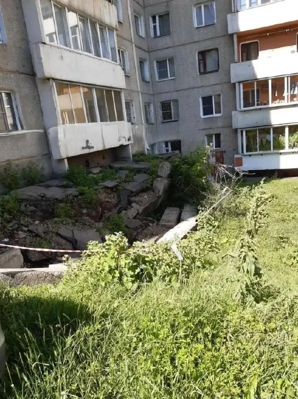 Под балконами образовался глубокий провал: бетонные плиты ушли в грунт, опасную зону огородили только лентой. Управляющая компания обсуждала ремонт с мэрией, но сроков не называет.