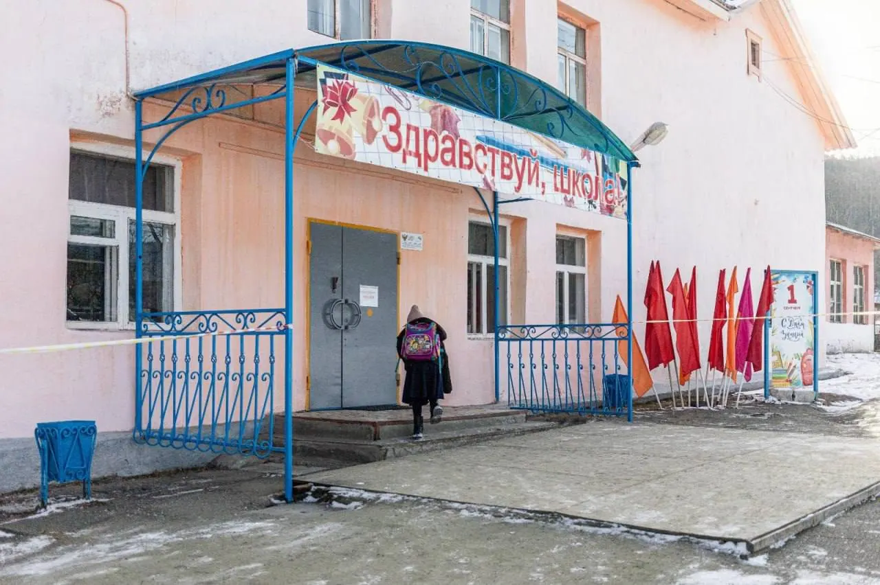 В Слюдянке Иркутской области продолжаются работы над новым школьным корпусом; старое деревянное здание рассчитано на 220 мест, сейчас там учатся 500 детей. В коридоре на стене — школьные парты, но без ножек: крышки превратили в памятные доски.